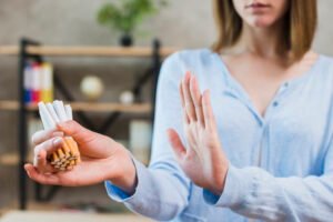 Wanita menunjukkan gestur stop sambil memegang rokok, konsep hipnoterapi berhenti merokok Bali