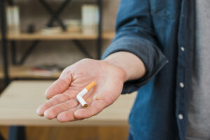 Tangan pria memegang rokok patah, gambaran hipnoterapi berhenti merokok Bali