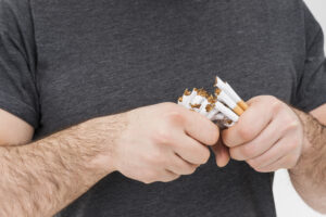 Pria mematahkan rokok dengan tangan sebagai simbol hipnoterapi berhenti merokok Bali